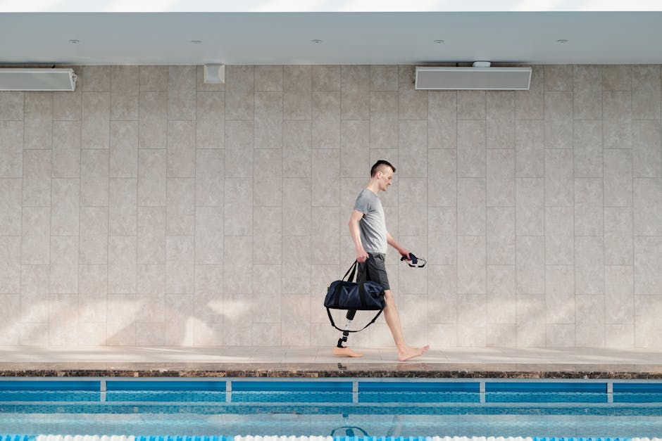 A determined amputee with a prosthetic leg walking confidently by a swimming pool indoors.